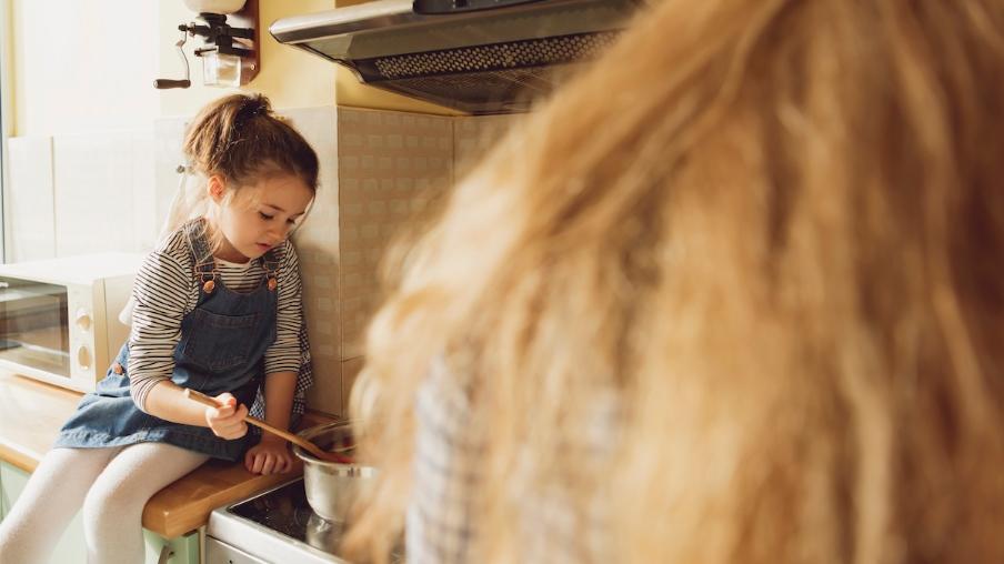 
		A girl is sitting on the kitchen counter and cooking with her mother
	